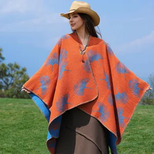 Detailaufnahme des orangefarbenen Strickponchos mit blauen Ginkgoblatt-Mustern im Freien.