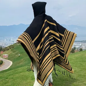 Back view of a black and gold striped hooded knit shawl with tassels in a scenic outdoor setting