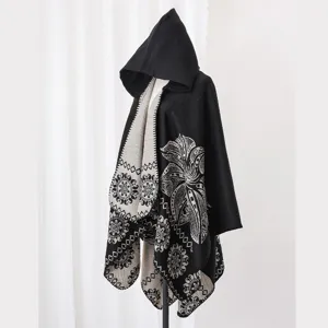 Detailansicht eines schwarzen Ponchos mit Kapuze und eleganten weißen Blumenmustern.