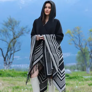 Outdoor view of a black hooded knitted poncho shawl with grey geometric stripes and tassels