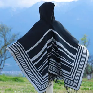 Back view of a warm striped hooded knit poncho with fringe details in a nature setting