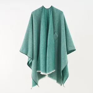 Detail of an elegant green knit poncho shawl with soft fringe edges and a textured finish.