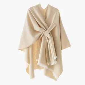 Close-up of beige knit poncho featuring a diagonal crossover tie and fringe hem details.