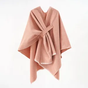 Close-up view of a peach knit poncho featuring a stylish diagonal strap and soft frayed edges
