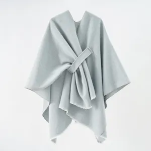 Close-up of a minimalist light grey knitted shawl with wrap-around tie and fringed edges