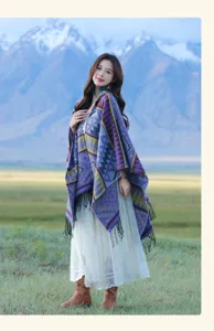 Frau trägt einen bunten Boheme-Kapuzen-Strickponcho mit Fransen in einer Berglandschaft.