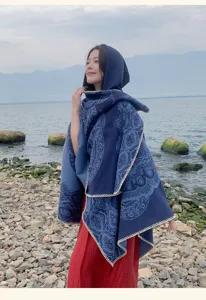 Detailaufnahme eines blauen ethnischen Kapuzenschals vor einer malerischen Seekulisse.