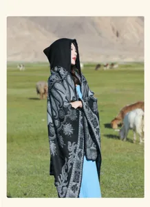 Model trägt einen schwarzen Strickschal mit Kapuze und Paisleymuster in einer Wiese