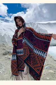 Bohemien-Strickponcho mit Kapuze und geometrischen Mustern in einer verschneiten Bergkulisse.