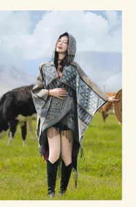 Model trägt einen Boheme-Strickponcho mit Kapuze und Quasten in einer Berglandschaft.