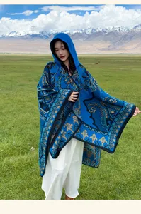Scialle in maglia con cappuccio blu stile etnico indossato in un paesaggio montano