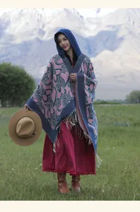 Mannequin portant un poncho à capuche avec motifs de cœurs roses dans un paysage alpin