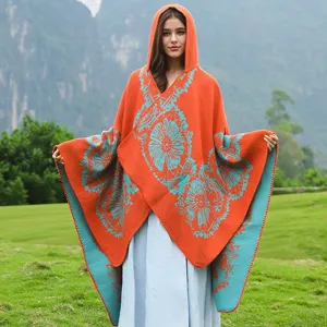 Detail des orangefarbenen Strick-Ponchos mit Kapuze und türkisen Blumenmustern.