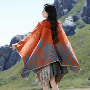 Back view of an orange knitted hooded poncho with blue floral patterns in a mountain setting