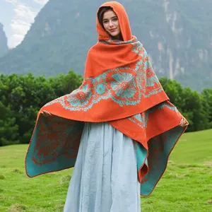 Frau trägt ein orangefarbenes Strick-Cape mit Kapuze und Blumenmuster in natürlicher Umgebung