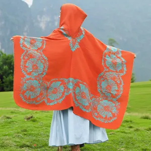 Detailansicht eines orangefarbenen Strickponchos mit Kapuze und cyanblauen Blumen