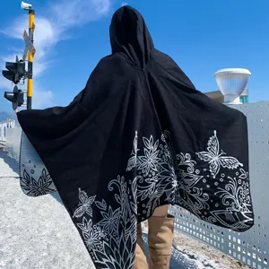 Detail view of black hooded knitted poncho featuring elegant white butterfly patterns