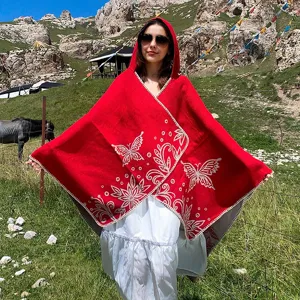 Red hooded knit poncho with butterfly patterns worn in an outdoor mountain landscape.