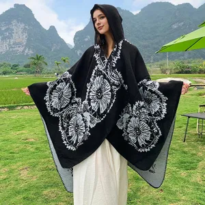 Ganzkörperansicht eines schwarzen Strickponchos mit Kapuze und Blumenmustern im Freien
