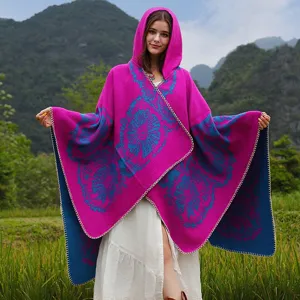 Eine Frau trägt einen lebhaften pink-blauen Kapuzen-Strickponcho in einer Bergwiese