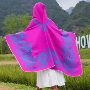 Detailansicht eines pinkfarbenen Strickponchos mit Kapuze und türkisen Blumenmustern.