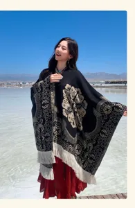 Detailansicht eines schwarzen Ethno-Ponchos mit weißen Jacquard-Blumenmustern und Fransen