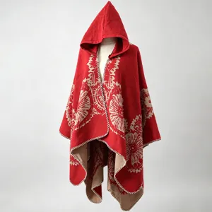 Detailansicht des roten Strick-Ponchos mit Kapuze und Blumenmuster auf einer Puppe