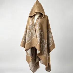 Detailansicht des beigen Strickponchos mit Kapuze und Blumenmuster auf grauem Hintergrund.