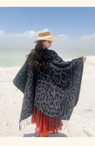 Back view of leopard print knitted shawl with tassels on a model in a scenic beach setting