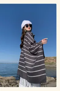 Thick striped knitted shawl with tassels worn by model in a scenic travel setting.