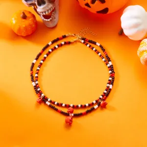 Detalle del conjunto de collar de cuentas de Halloween con calaveras rojas sobre fondo naranja