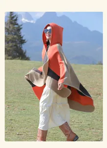 Model wearing ethnic striped hooded poncho walking against scenic mountain backdrop