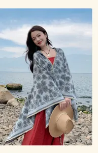 Detail eines grau gestrickten Kapuzenponchos mit Herzmuster, getragen an einem Felsstrand