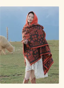 Frau trägt Ethno-Strickponcho mit Kapuze und Herzmuster in einer Graslandschaft