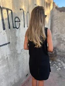 Detailed view of casual black sleeveless linen dress worn by model outdoors against wall.