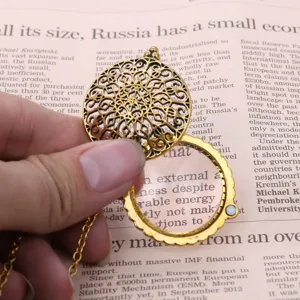 Close-up of vintage hollow magnifying glass pendant necklace on newspaper background