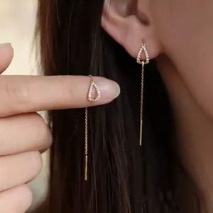 Close-up detail of gold teardrop threader earrings with zircon tassels worn on ear.