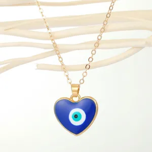 Close-up detail of a heart-shaped blue evil eye pendant on a gold-colored chain.