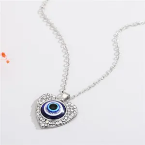 Close-up of silver-toned heart pendant necklace featuring an evil eye motif and crystals.