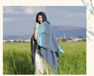 Buitenfoto van een vrouw met een blauwe gradient sjaal met capuchon en franjes aan de rand.
