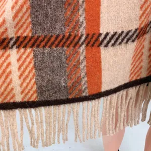 Detailaufnahme des Karomusters eines Ponchos mit Fransen in warmem Orange und Beige.
