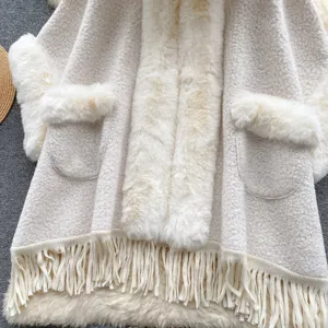 Detailaufnahme eines cremefarbenen Bouclé-Umhangs mit Kunstpelzbesatz und Fransen