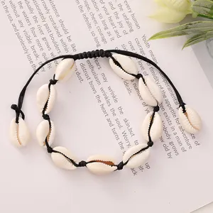 A detailed macro view of a bohemian woven cowrie shell bracelet lying on a book background.