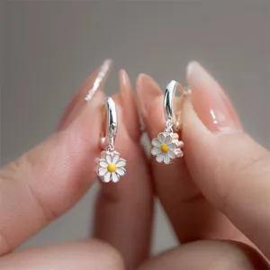 Macro shot of silver hoop earrings with white enamel daisy charms held by hand.