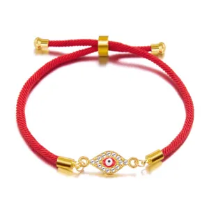 Close-up detail of a red braided rope bracelet featuring a gold rhinestone evil eye charm.