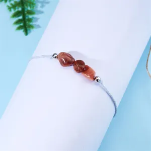 Primer plano de cuentas de jaspe rojo irregulares en una pulsera de cordón azul trenzado claro