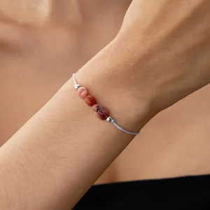 Detalle de una pulsera tejida con tres piedras de nacimiento naturales rojas e irregulares