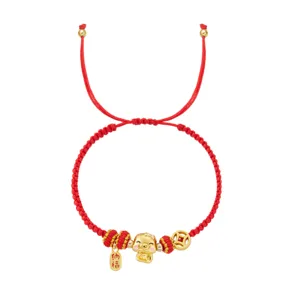 Vue détaillée d'un bracelet tressé rouge avec un pendentif doré porte-bonheur et tag.