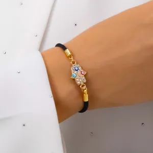 Detailed view of gold Hamsa hand bracelet with inlaid Evil Eye crystals and black cord
