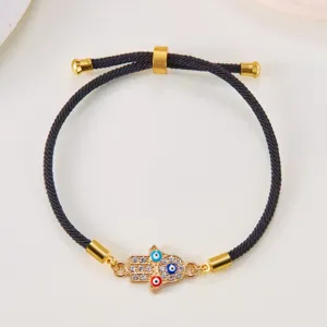 Detailed view of adjustable black rope bracelet with gold Hamsa Hand and Evil Eye charms